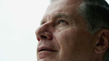 Fototapeta premium Contemplative older man close-up face looking up at sky with thoughtful expression, person closing eyes in meditation