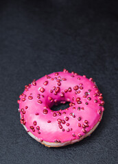 Pink sweet donut with pink frosting on the black background. Vertical photo of delicious berry doughnut.