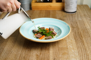 Hand Pouring Beef Soup into a Plate on a wooden table