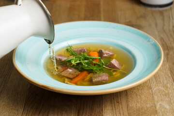 Pouring Beef Soup into a Plate on a wooden table