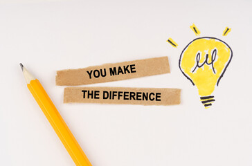 On a white surface, a luminous light bulb and pieces of paper with the inscription - You Make The...