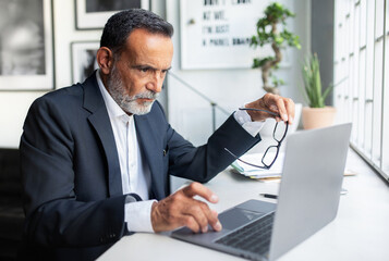Obraz premium Focused sad confident european old businessman in suit looks at laptop, create idea in office