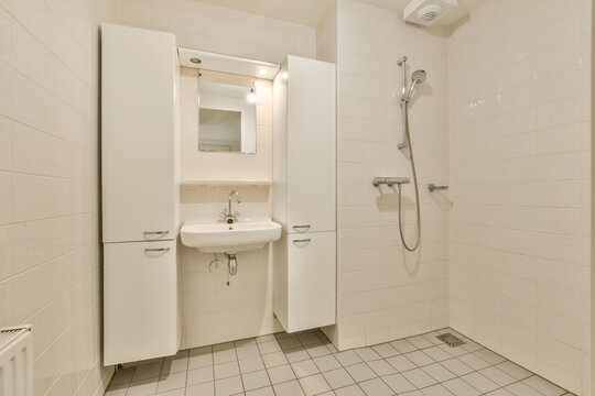 a bathroom with white tiles on the floor and walls, including a sink, mirror, shower stall and towel rack