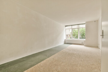 an empty room with white walls and green flooring on the right side, there is a window to the left