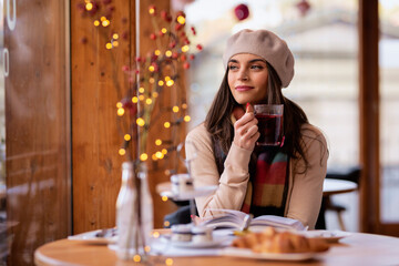 Beautiful woman wearing beret hat and scarf whle sitting in a cafe and reading a book