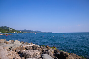 Tranquility rocky beach with big black stones, blue sea and sky as background, tranquil and looks beautiful.Big stone beach in front of sea with sky