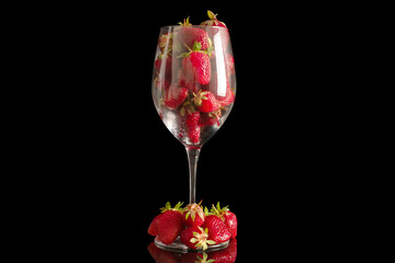 Several red strawberries in a glass goblet, macro, isolated on black background.