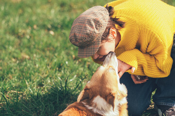 Portrait of a caucasian woman in yellow sweater and checkered cap with corgi dog