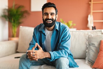 Happy indian man relaxing sitting on couch at modern home
