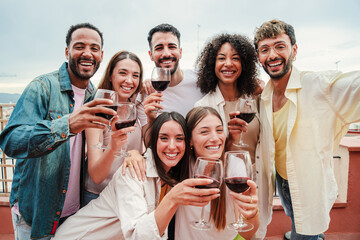 Group of cheerful best friends on a rooftop wine party. Crowd of young people drinking, toasting glasses, laughing and having fun on a friendly meeting, enjoying happy hour at winery bar restaurant