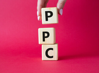 PPC - Pay Per Click symbol. Wooden cubes with words PPC. Businessman hand. Beautiful red background. Business and PPC concept. Copy space.