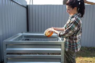 A woman in a plaid shirt pours food waste from a bowl into a compost heap of potato and carrot...