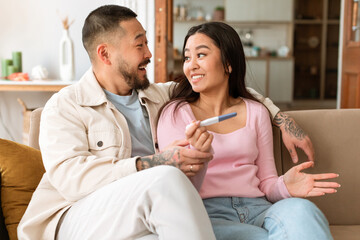 Happy Japanese Spouses Holding Positive Pregnancy Test Sitting At Home