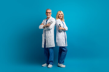 Friendly senior doctors in medical workwear posing on blue