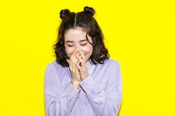 A woman covers her mouth with her hands isolated on yellow background
