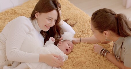 Active time of the kid, communication parents. Two young women look at a newborn, talking, smiling. Baby's first days at home. Couple has won the right to adopt a child.