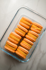 Sweet orange French or Italian macarons with mango ganashe in transparent glass package. View from above