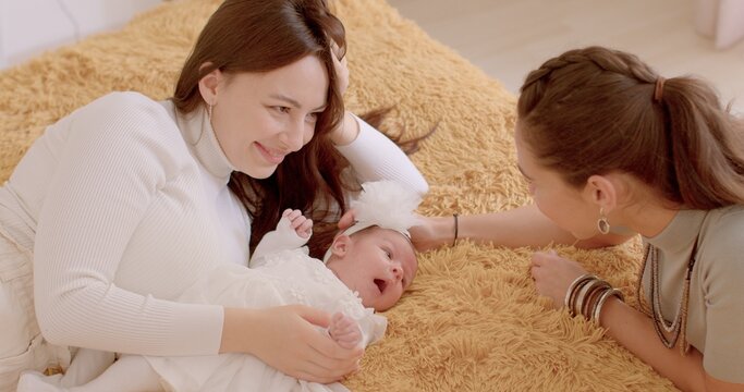 Active time of the kid, communication parents. Two young women look at a newborn, talking, smiling. Baby's first days at home. Couple has won the right to adopt a child. - Powered by Adobe