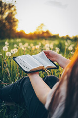 Christian woman holds bible in her hands. Reading the Holy Bible in a field during beautiful sunset. Concept for faith, spirituality and religion. Peace, hope