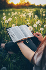 Christian woman holds bible in her hands. Reading the Holy Bible in a field during beautiful...