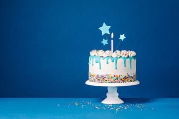 White birthday drip cake with teal ganache, star toppers and fun candles over dark blue background - 613308294