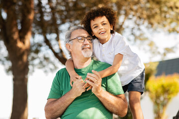Happy black little boy hugging senior man with beard, have fun, relax in park at weekend, outdoor