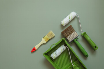 Wall paint roller and brush on green background, top view