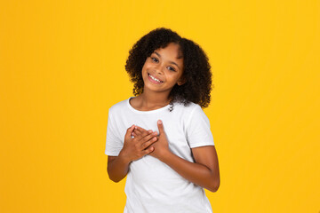 Satisfied glad curly teenager black girl in white t-shirt presses hands to chest, says thank