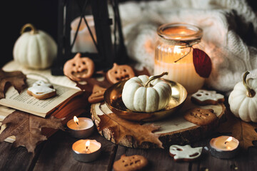 Autumn home composition with aromatic candle, pumpkin, wool sweater, halloween homemade cookies. Aromatherapy on a grey fall morning, atmosphere of cosiness and relax. Holiday handmade decor