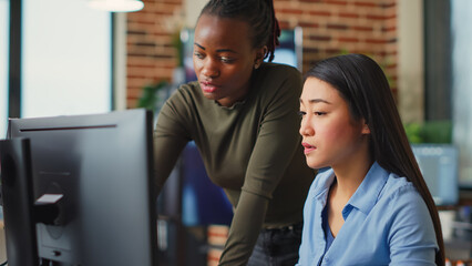 Multiethnic team of IT developers working on computers to create artistic machinery software, using...