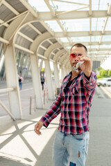 a handsome man nicely and stylishly dressed in pink glasses stands at a bus stop