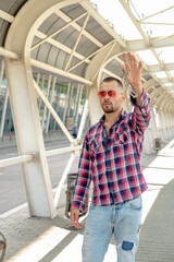 a handsome man nicely and stylishly dressed in pink glasses stands at a bus stop