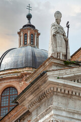 Urbino, Italy, 2023, May 5: Sant Agostino statue, on the Santa Maria Assunta cathedral roof. In the background, the dome.