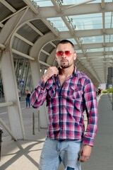 a handsome man nicely and stylishly dressed in pink glasses stands at a bus stop