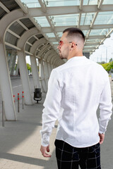 a handsome man nicely and stylishly dressed in pink glasses stands at a bus stop