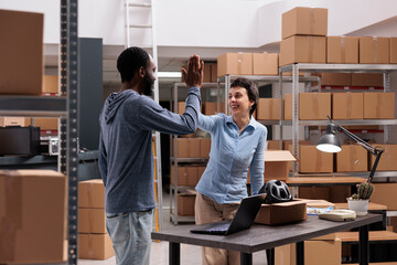 Happy storehouse employees doing high five after finishing putting helmet packages in cardboard...