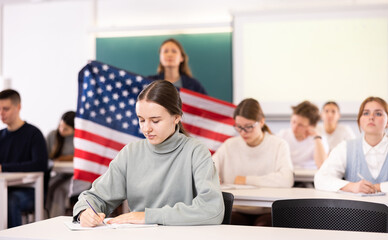 Geography lesson in school class - teacher talks about United States of America, holding a flag in...