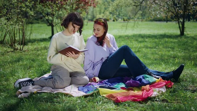 Attractive lesbian couple feeling so happy together at the picnic laying down on the sofa they eating some fruits and write something on the notes in the middle of nature