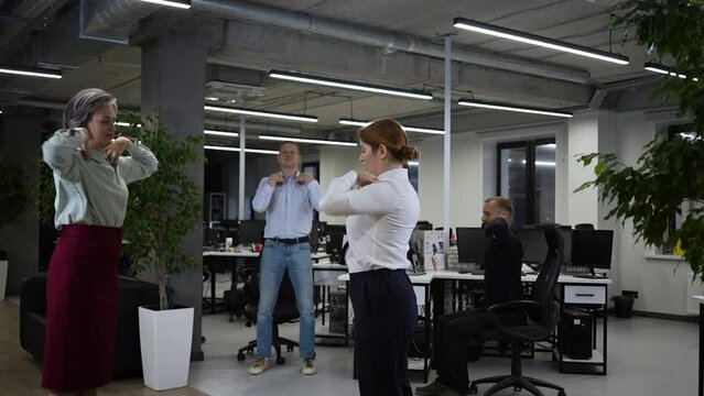 Four office workers warm up during a break. Employees do fitness exercises at the workplace. Slow motion. 