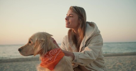 Portrait of a young blonde girl who strokes her dog in the morning on the seashore. Morning walk with a pet on the beach at sunrise