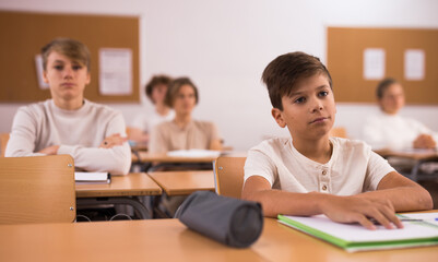 Teen boy listening to lecturer and writing in notebook in classroom