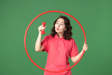front view young saleswoman holding hula hoop and dumbbell on green background color yoga body...