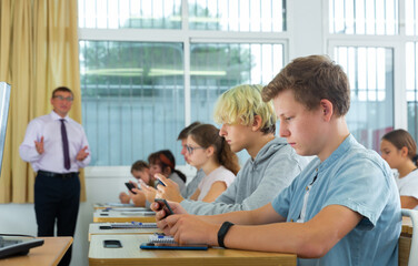 Fototapeta premium Group of modern teenagers sitting with mobile phones on lesson in classroom