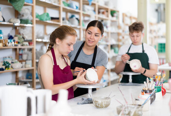 Woman master potter teaches teen girl how to draw and glaze pottery