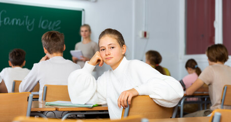 Bored teenage girl turned around and looking at camera during lesson in school.