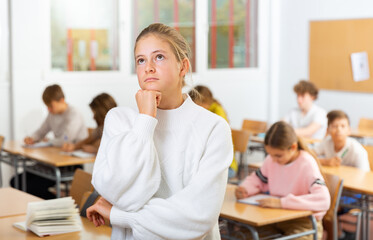 Fototapeta premium Upset girl stands in a school class against the background of classmates