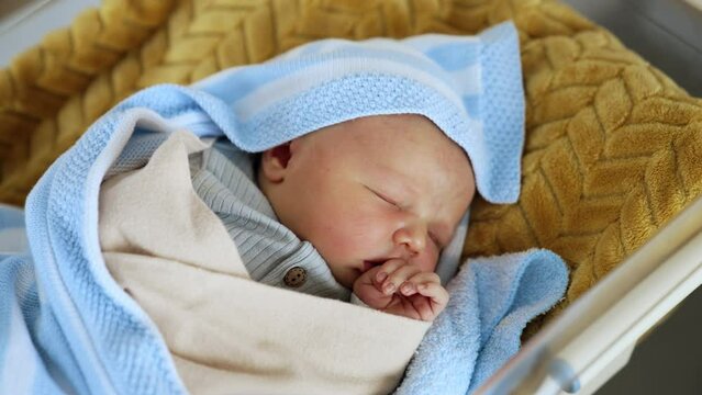 Adorable baby sleeping peacefully in the crib. Newborn child in blankets sleeps holding hand at his mouth. Top view close up.