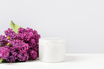 Cosmetic bottle container on a gray background lilac flowers. Top view of mockup of white bottle plastic tube for branding of cosmetics gel, cream, skin care.