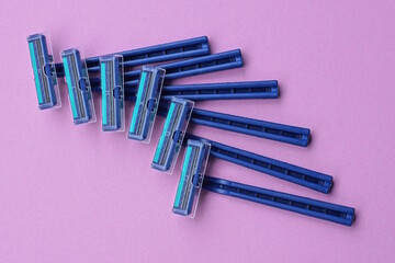 a set of six blue plastic razors lie on a pink table