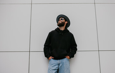 City portrait of handsome hipster guy with beard wearing black blank hoodie or sweatshirt with...